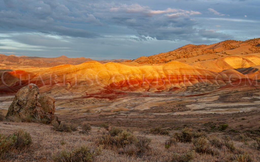 The Painted Hills in Central Oregon's High Desert glow orange as the setting sun peeks through the storm clouds.